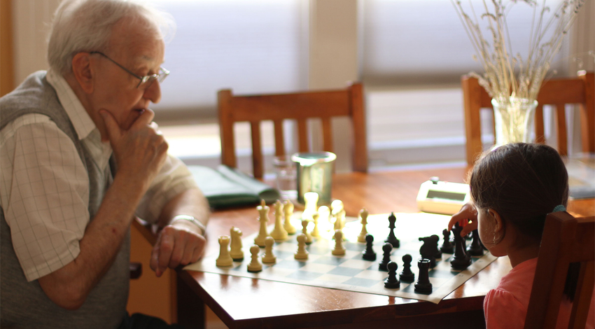 Elderly man teaching young child chess